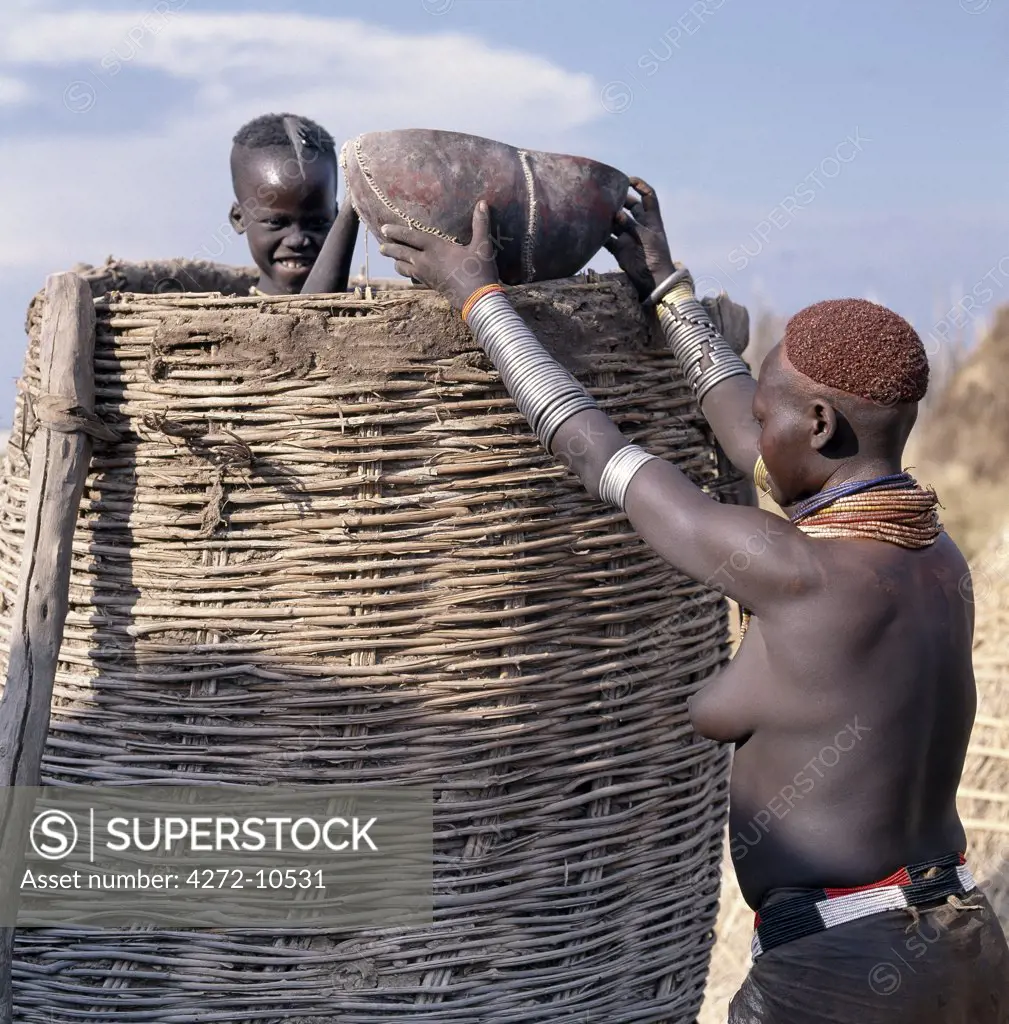 A Karo woman is helped by a member of her family to take grain out of a traditional granary in the village of Duss. The Karo are a small tribe living in three main villages along the lower reaches of the Omo River in southwest Ethiopia.