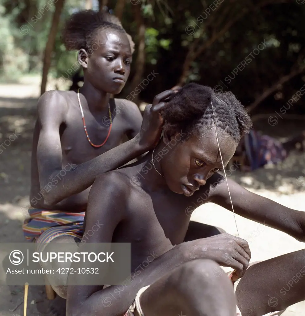 A Karo youth braids the hair of his friend in the shade of trees lining the banks of the Omo River. The Karo are a small tribe living in three main villages along the lower reaches of the Omo River in southwest Ethiopia.