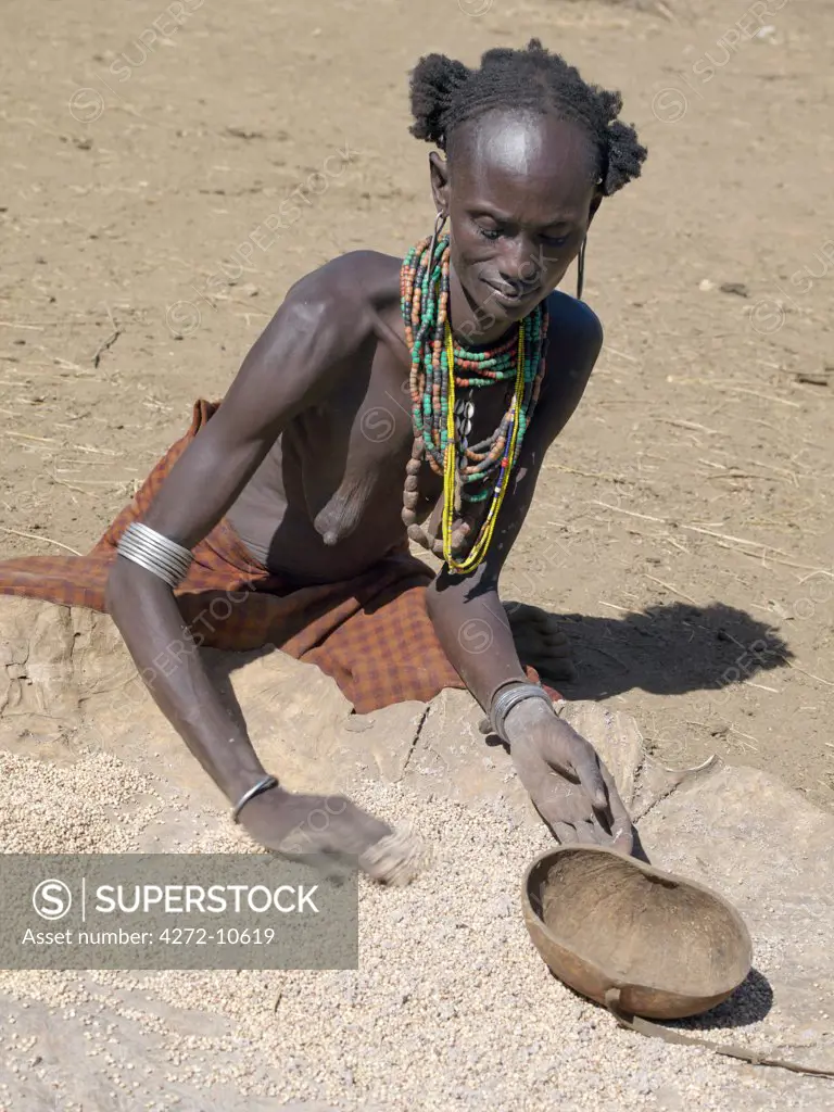 A Dassanech woman spreads sorghum on an oxhide to dry it.The Dassanech speak a language of Eastern Cushitic origin. They live in the Omo Delta and they practice animal husbandry and fishing as well as agriculture.