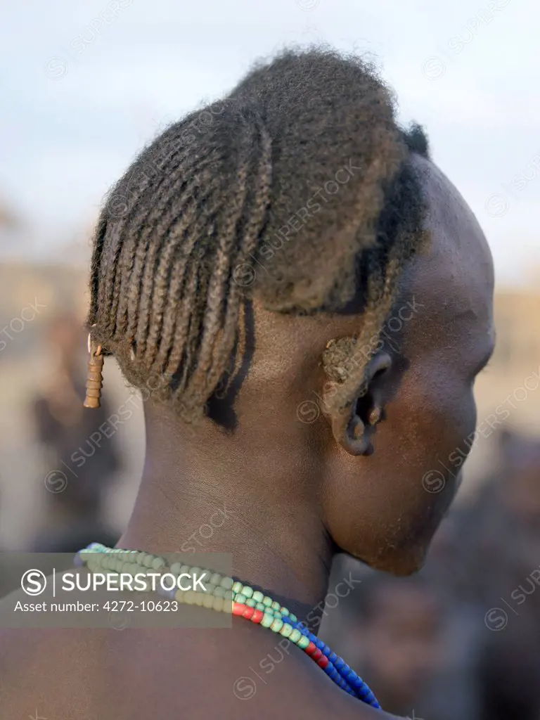 A finely braided hairstyle of a young Dassanech man. Note the quid of chewing tobacco behind his right ear.  Most adult Dassanech chew local tobacco.The Omo Delta of southwest Ethiopia is one of the least accessible and least developed parts of East Africa.