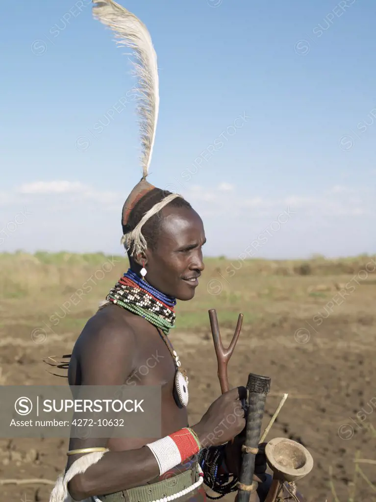 A smartly dressed Dassanech man stand on a bank of the Omo River.   Their attire signifies that they are about to marry.  Note the oryx horns they are carrying in which they keep their ostrich feathers for adorning their clay hairdos.The Omo Delta of southwest Ethiopia is one of the least accessible and least developed parts of East Africa.