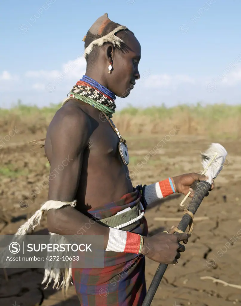 A smartly dressed Dassanech man stand on a bank of the Omo River.   Their attire signifies that they are about to marry.  Note the oryx horns they are carrying in which they keep their ostrich feathers for adorning their clay hairdos.The Omo Delta of southwest Ethiopia is one of the least accessible and least developed parts of East Africa.