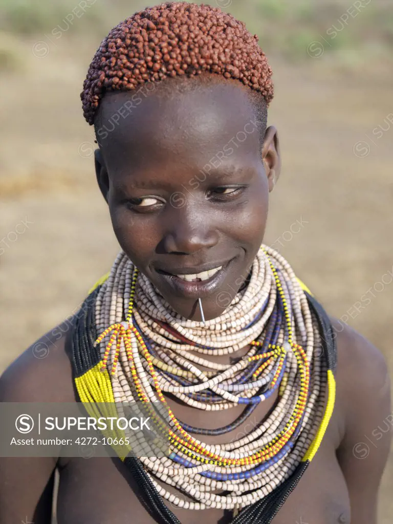 A Karo girl in all her finery.  It is a Karo tradition for girls and young women to pierce a hole below the lower lip in which they place a thin piece of metal or a nail for decoration. The Karo are a small tribe living in three main villages along the lower reaches of the Omo River in southwest Ethiopia.
