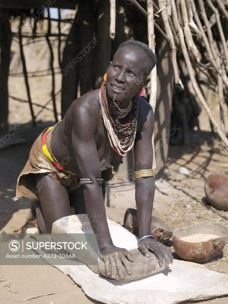 A Karo woman grinds sorghum using a traditional flat grinding stone.  It is a Karo tradition for girls and young women to pierce a hole below the lower lip in which they place a thin piece of metal or a nail for decoration.The Karo are a small tribe living in three main villages along the lower reaches of the Omo River in southwest Ethiopia.