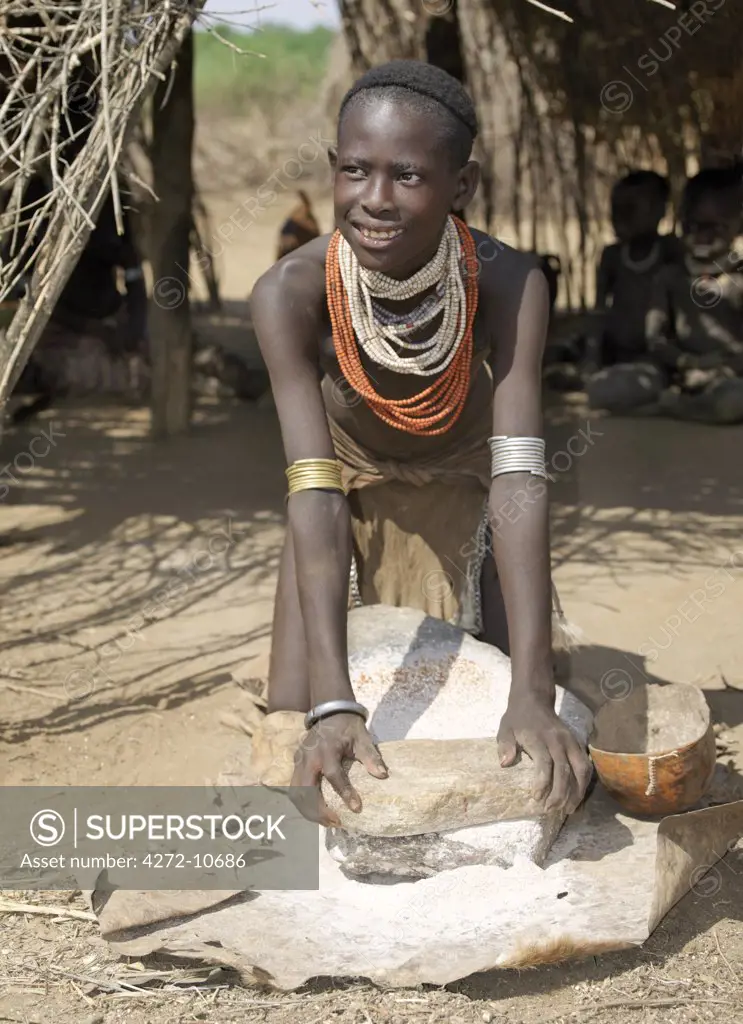A Kwegu girl grinds sorghum using a flat grinding stone. The Kwegu are the smallest tribe living on the banks the Omo River in southwest Ethiopia.