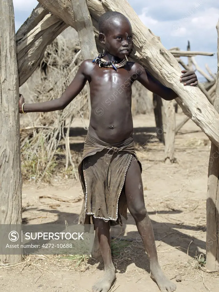A young Kwegu girl stands among dry wood poles at her familys home. Adopting the practice of Karo women and girls, many Kwegu girls pierce a hole below the lower lip in which they place a thin piece of metal or a nail for decoration. The Kwegu are the smallest tribe living on the banks the Omo River in southwest Ethiopia.