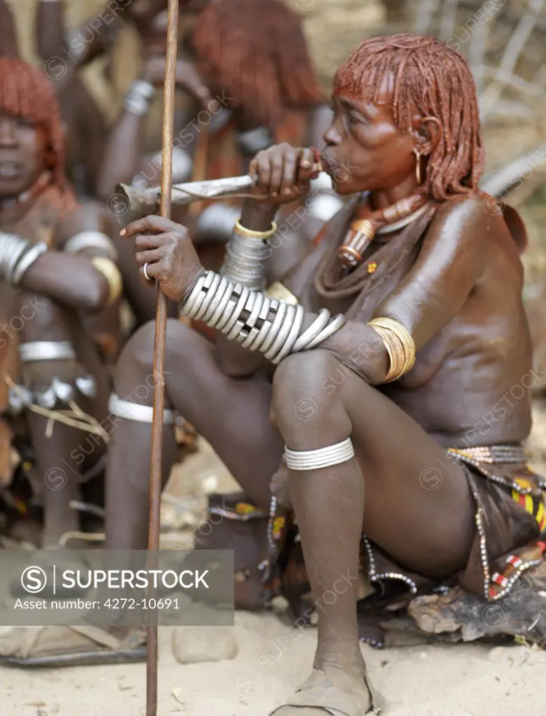 A Hamar woman blows a tin trumpet at a Jumping of the Bull ceremony. The Hamar are semi nomadic pastoralists of Southwest Ethiopia whose women wear striking traditional dress and style their red ochred hair mop fashion.