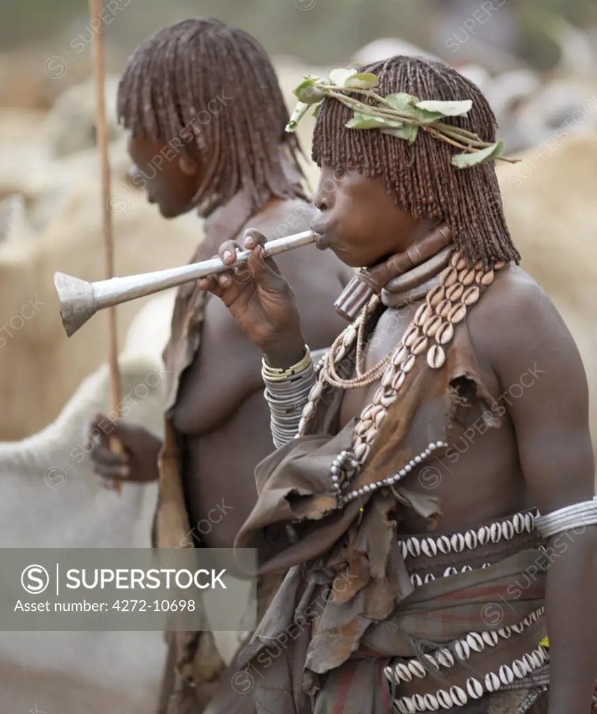 A Hamar woman blows a tin trumpet at a Jumping of the Bull ceremony. The Hamar are semi nomadic pastoralists of Southwest Ethiopia whose women wear striking traditional dress and style their red ochred hair mop fashion.