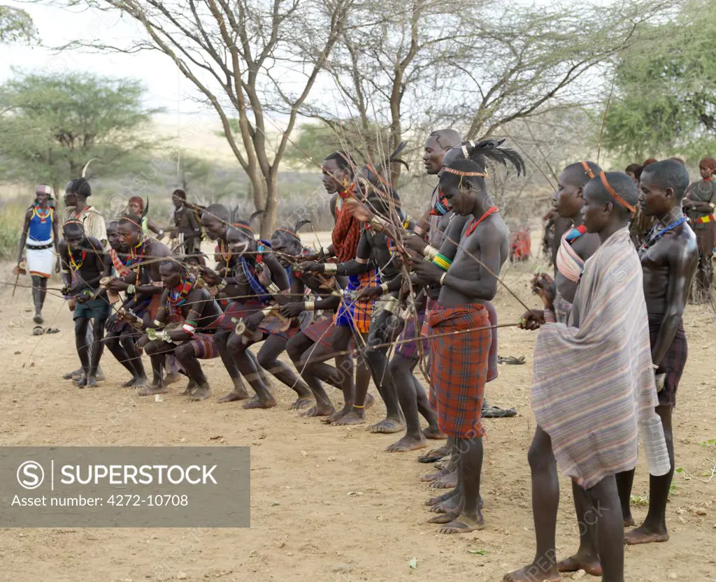 With whipping sticks in their hands, men crouch as they bless an initiate who is about to perform his Jumping of the Bull ceremony. The Hamar are semi nomadic pastoralists of Southwest Ethiopia who embrace an age grade system that includes several rites of passage for young men.
