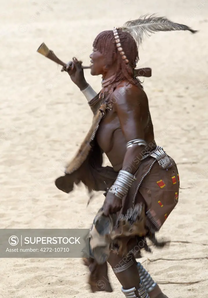 An old Hamar woman dances and blows a trumpet at a Jumping of the Bull ceremonyThe The Hamar are semi nomadic pastoralists of Southwest Ethiopia whose women wear striking traditional dress and style their red ochred hair mop fashion.
