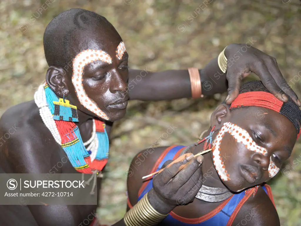A Hamar man with an unusual hairstyle decorates a girls face before the start of a Jumping of the Bull ceremony.The semi nomadic Hamar of Southwest Ethiopia embrace an age grade system that includes several rites of passage for young men.