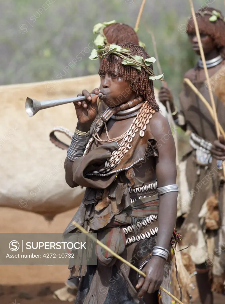 A Hamar woman blows a tin trumpet at a Jumping of the Bull ceremony. The semi nomadic Hamar of Southwest Ethiopia embrace an age grade system that includes several rites of passage for young men.