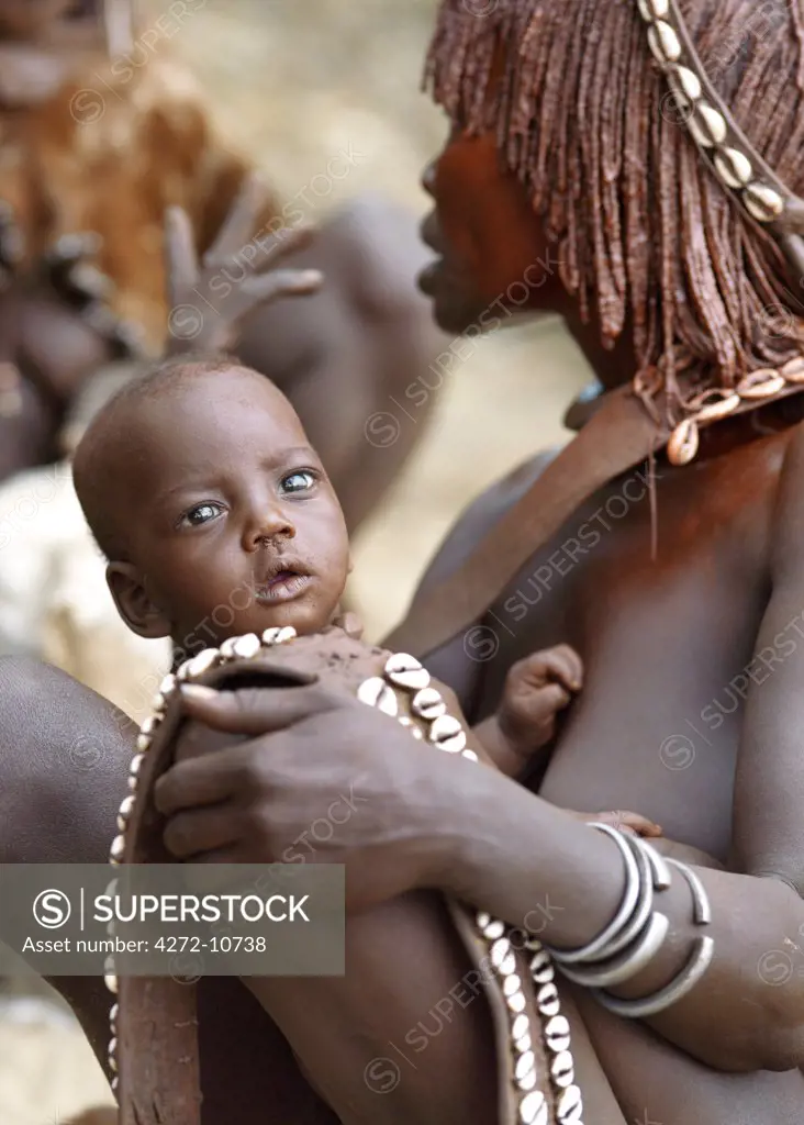A Hamar woman holds her baby in her arms.,The Hamar are semi-nomadic pastoralists of Southwest Ethiopia whose women wear striking traditional dress and style their red-ochred hair mop-fashion.  Skins are widely used for clothing and cowrie shells are popular adornments yet the sea is 500 miles from their home.