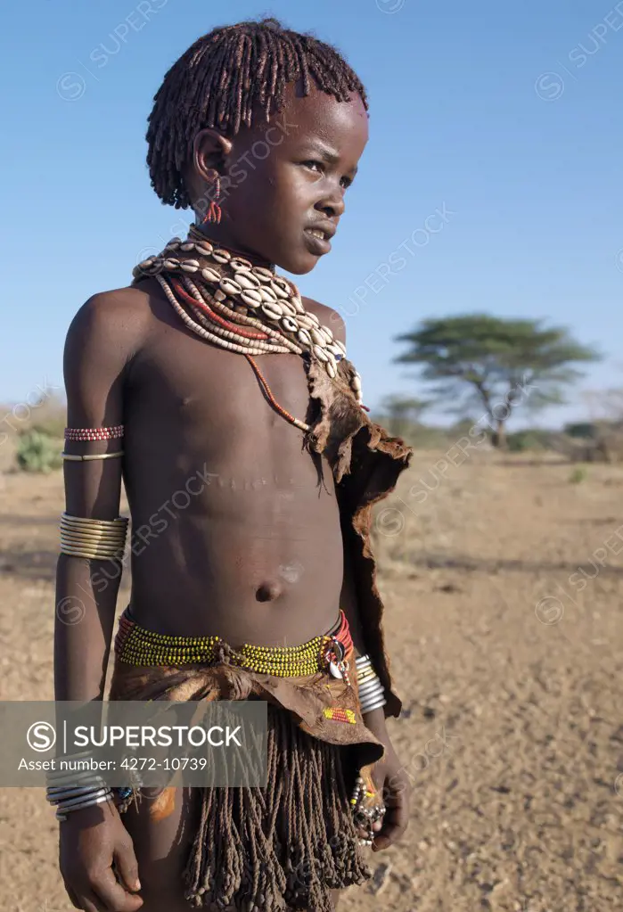 A Hamar girl in traditional attire.  Her leather skirt is made from the twisted strands of goatskin.  Cowries are always popular to embellish a woman's or girl's appearance.The Hamar are semi-nomadic pastoralists who live in harsh country around the Hamar Mountains of Southwest Ethiopia.