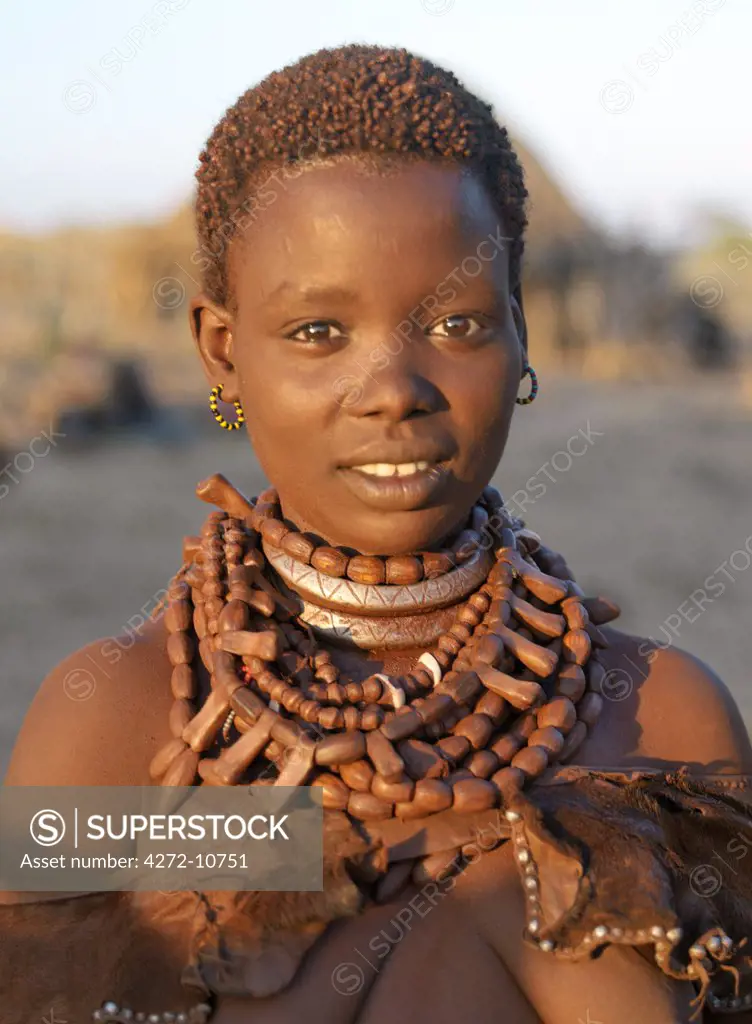 The ochre worn by a married Hamar girl glows deep red in the late afternoon light.;The Hamar are semi-nomadic pastoralists of Southwest Ethiopia whose women and girls wear striking traditional dress. Skins are widely used for clothing and heavy metal necklaces, bracelets and anklets form part of a woman's adornments. Cowries are also popular to embellish their appearance.