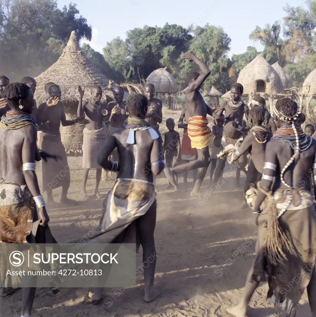 A lively Nyagatom dance is enjoyed by villagers in the late afternoon. The elevated houses in the background are both homes and granaries, which have been built to withstand flooding when the Omo River bursts its banks The Nyagatom are one of the largest tribes and arguably the most warlike people living along the Omo River in Southwest Ethiopia.