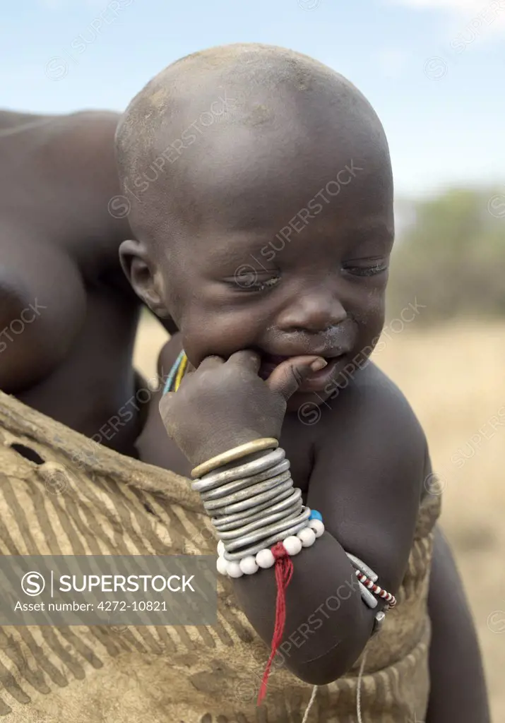 A Mursi child is carried safely in her mothers decorated leather garments. The Mursi speak a Nilotic language and have affinities with the Shilluk and Anuak of eastern Sudan.  They live in a remote area of southwest Ethiopia along the Omo River.