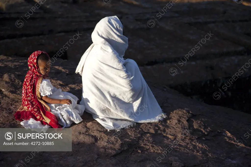 Ethiopia, Lalibela. A woman prays by Bet Giyorgis, whilst her daughter loses concentration.