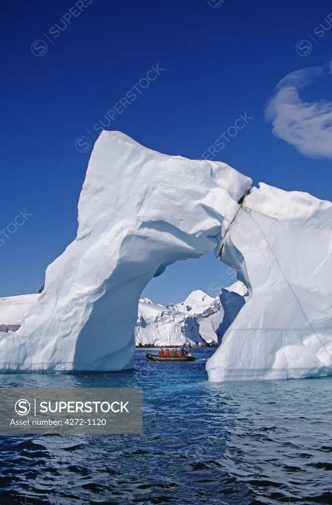 Antarctica, Grandidier Channel. Tourists Zodiac cruising by arched iceberg near Booth Island.