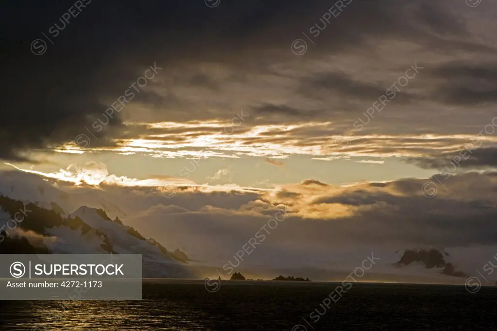 Antarctica, Antarctic Peninsula, Half Moon Bay. Heading out to sea from the penguin breeding beach and scientific station of Half Moon Bay at sunset with storm clouds breaking over the surrounding peaks.
