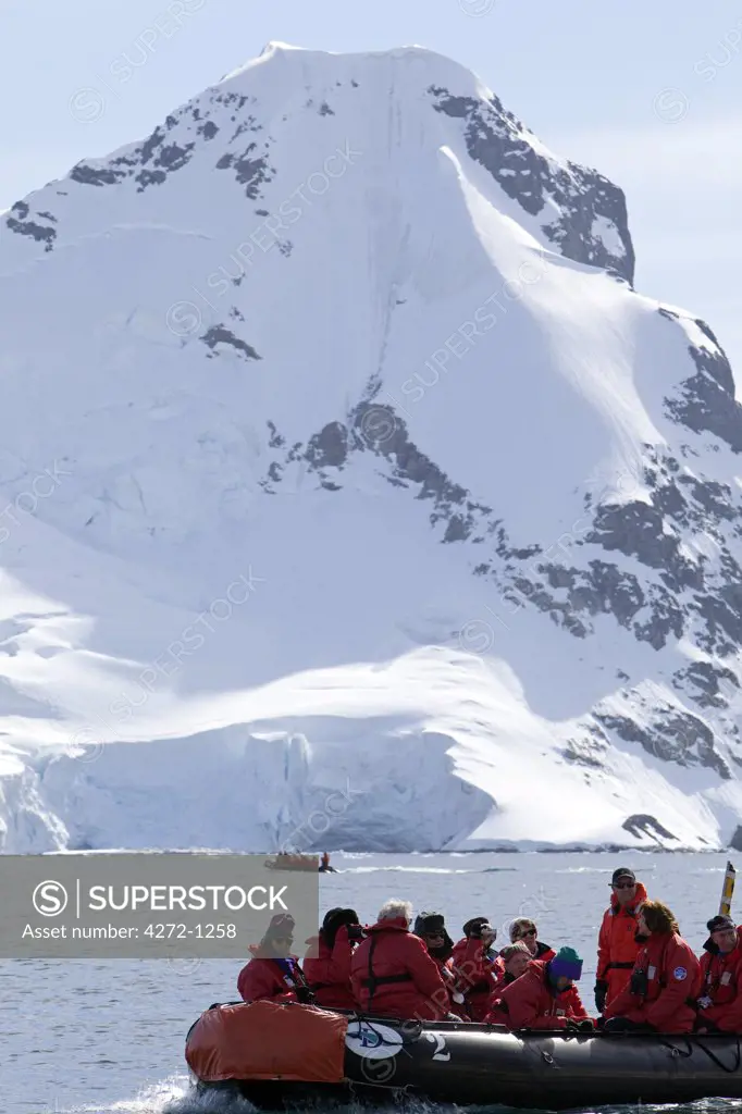 Antarctica, Antarctic Peninsula. An group of passengers dressed for operations in Antarctic waters passes underneath a heavily glaciated peak with a second zodiac in the background.