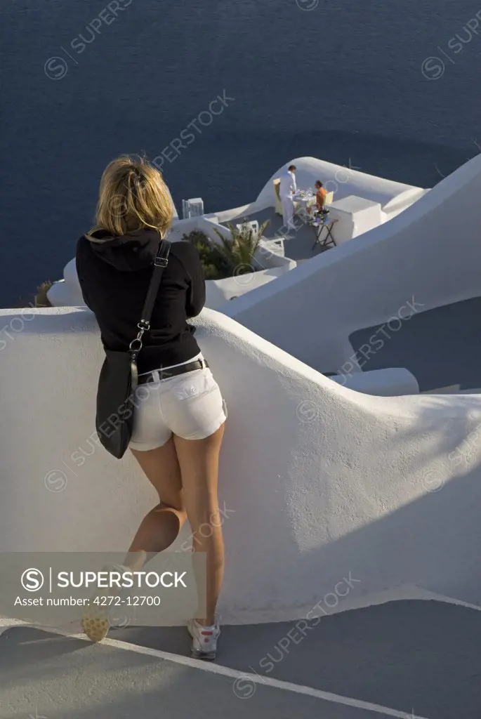 Greece, Santorini, Oia. A tourist looks out to sea from the cliff of Oia, where houses have been built into the porous volcanic rock.