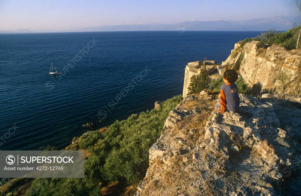Greece, Peloponnese, Messinia, Koroni. A young boy gazes down at the Mediterranean Sea from the lofty ramparts of Koroni's citadel, which was built by medieval Venetians.