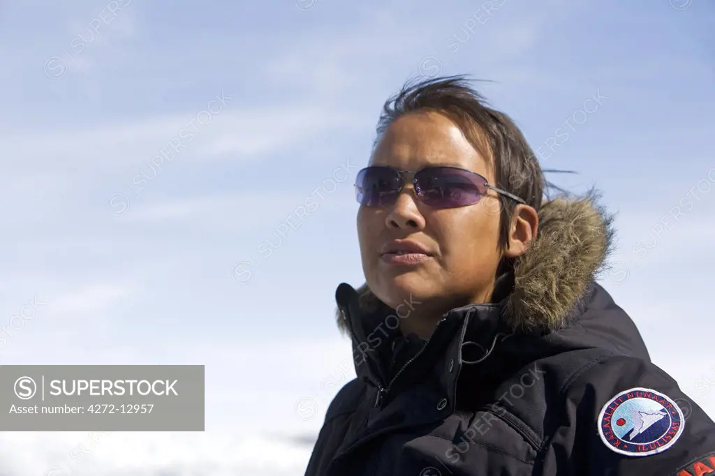 Greenland, Eqi Glacier. An attractive Greenlandic woman working as an adventure tour guide dressed in a parka with national badges.