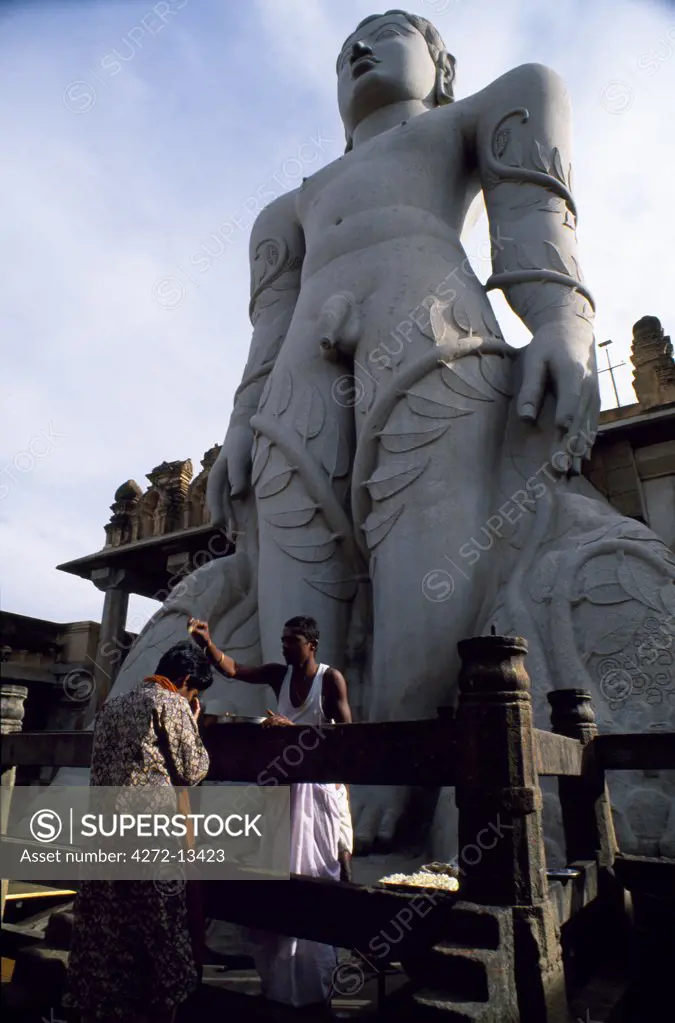 Pilgrim is anointed by an attendant as she prays beside the 18 metre tall statue of Gomateshvara, the largest free-standing sculpture in India
