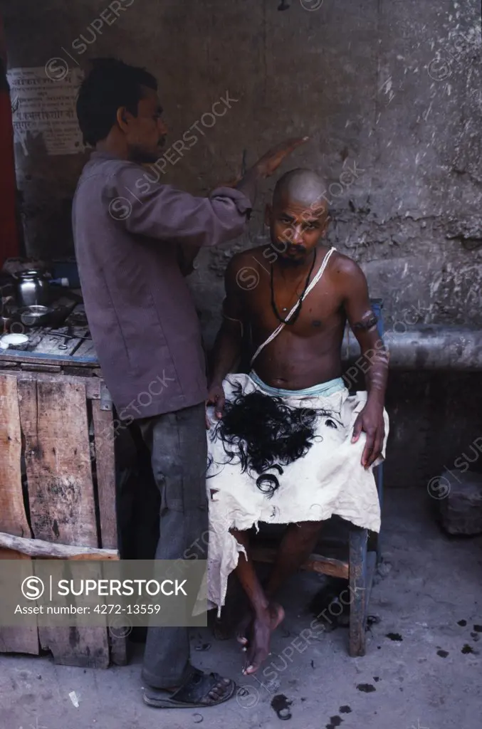 A Hindu pilgrim, his white thread indicating his Brahmin caste, has his head shaved before observing religious rites beside the Narmada River.