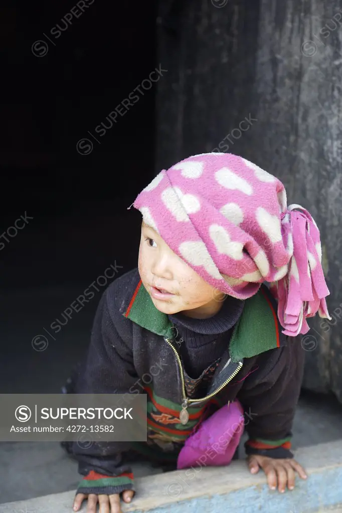 Small Indian girl in pink hat crawling out of door