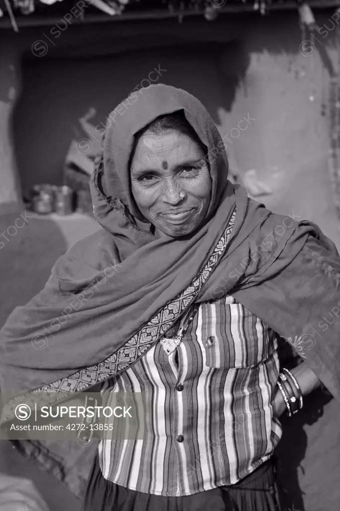 India, Rajasthan, Jaipur, Sariska.  The matriarch of the a small farming household takes a break from preparing lunch to pose for the camera.