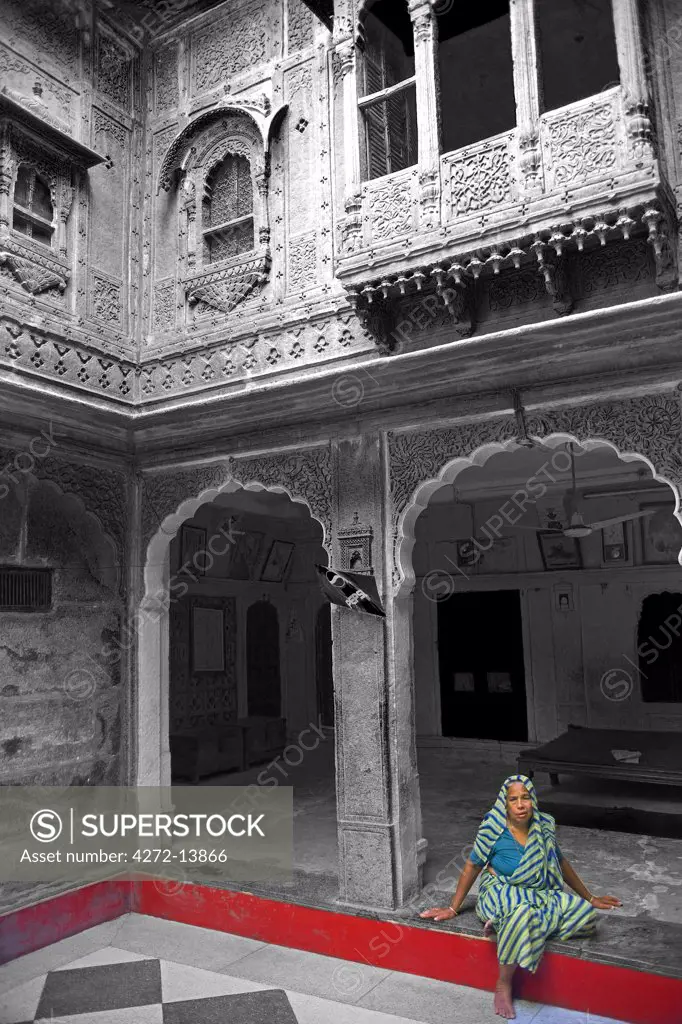 India, Rajasthan, Jaiselmer, Patwon ki Haveli. Traditionally dressed dressed lady relaxed in the main courtyard of one the cities best preserved Havelis.