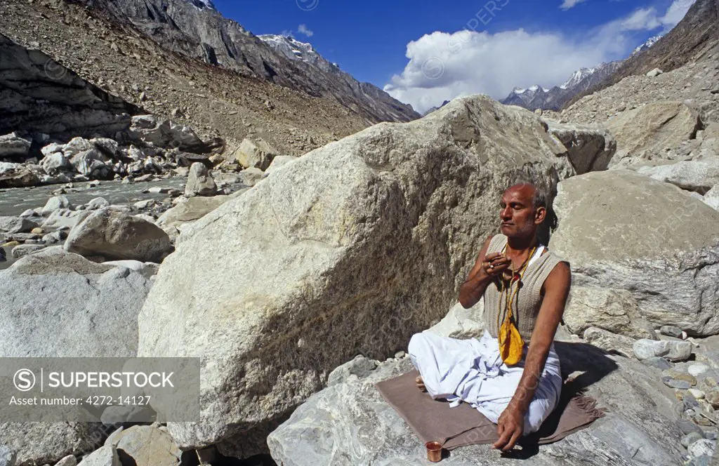 India, Uttarakhand, Garhwal, Gomukh, nr Gangotri. A pilgrim prays by the River Ganges near the snout of a glacier.