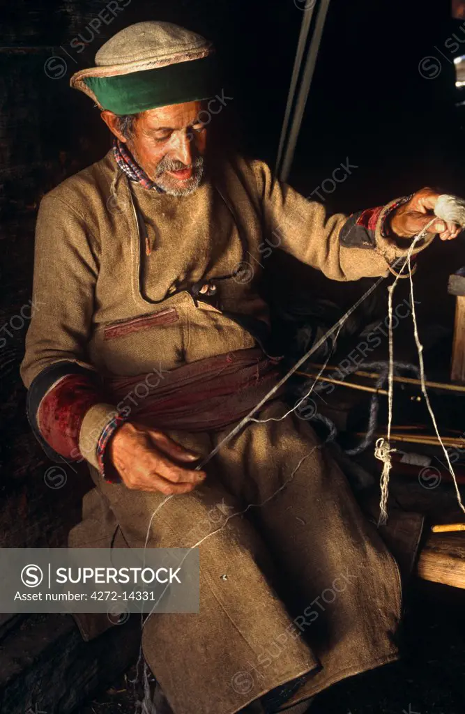 India, Himachal Pradesh, Kinnaur, Baspa Valley, Kamru. A Kinnauri man wearing a traditional Kinnauri hat prepares skeins of wool for weaving.