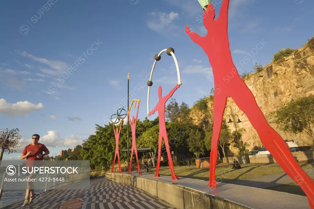 Australia, Queensland, Brisbane. An early morning jogger passes sculptures on the Brisbane waterfront near Kangaroo Point.