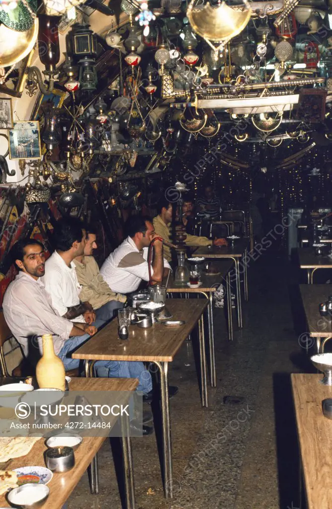 Iran, Esfahan. Men sit at tables drinking tea and smoking in a typical chai-kana or tea-house in central Esfahan