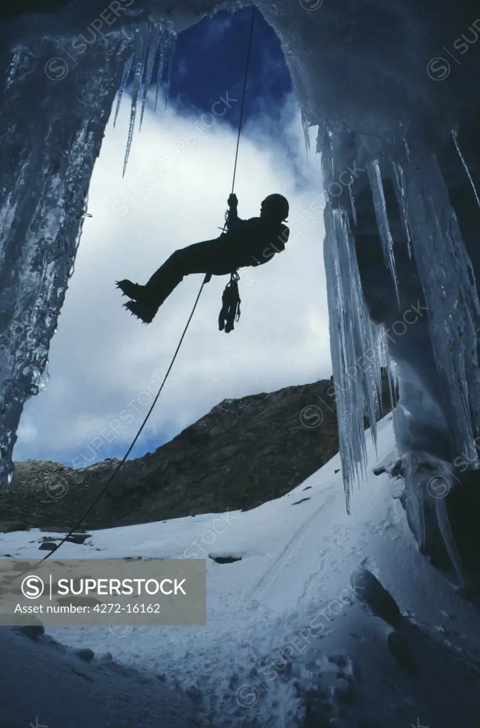 A climber abseils over the mouth of an ice cave at the foot of the Lewis Glacier.