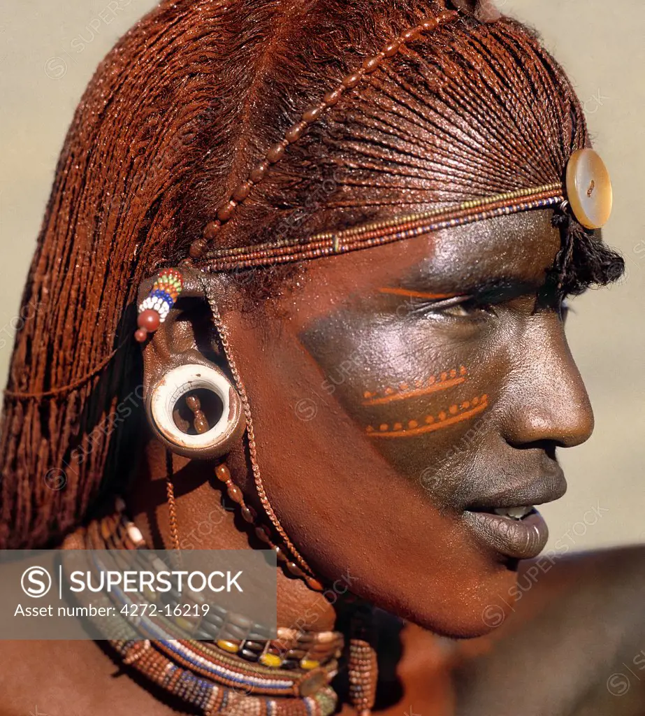 A Samburu warrior resplendent with long, braided, Ochred hair.  The round ear ornaments of the warriors are fashioned from ivory.  Samburu warriors are vain and proud, taking great trouble over their appearance. Ochre is a natural earth containing ferric oxide which is mixed with animal fat to the consistency of greasepaint.