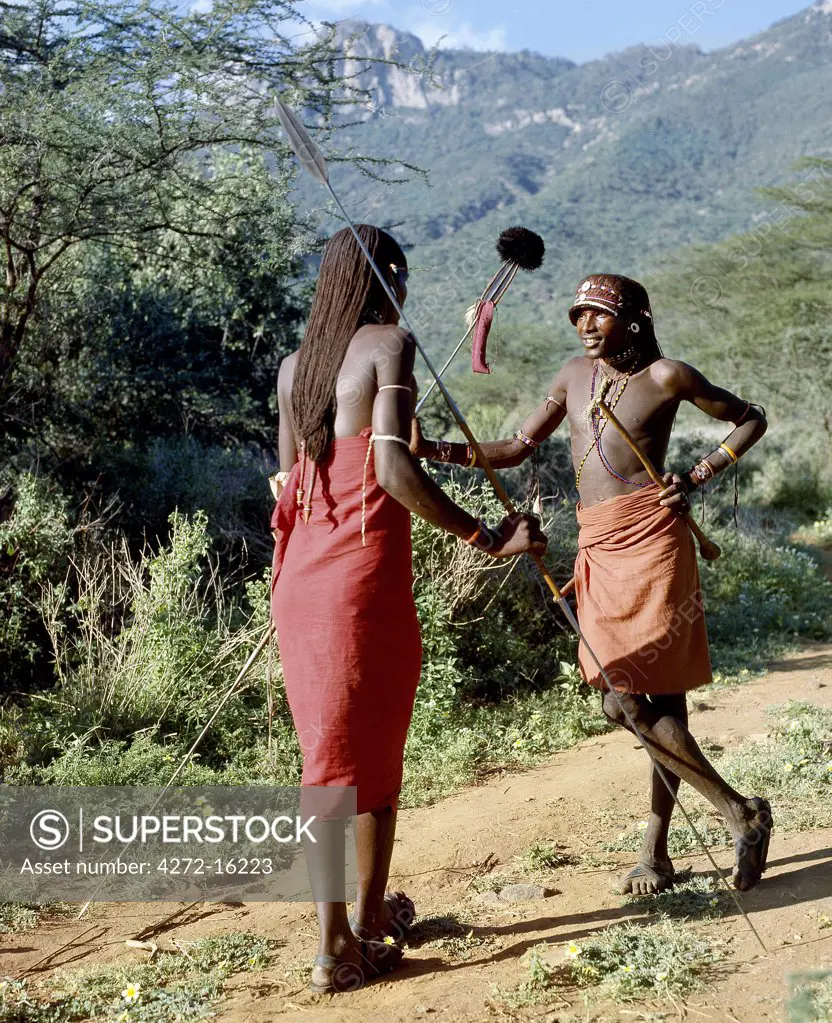 Two Samburu warriors converse, their long braids of Ochred hair distinguishing them from other members of their society.  Samburu warriors are vain and proud, taking great trouble over their appearance. An ostrich feather pompom decorates the top of a spear.