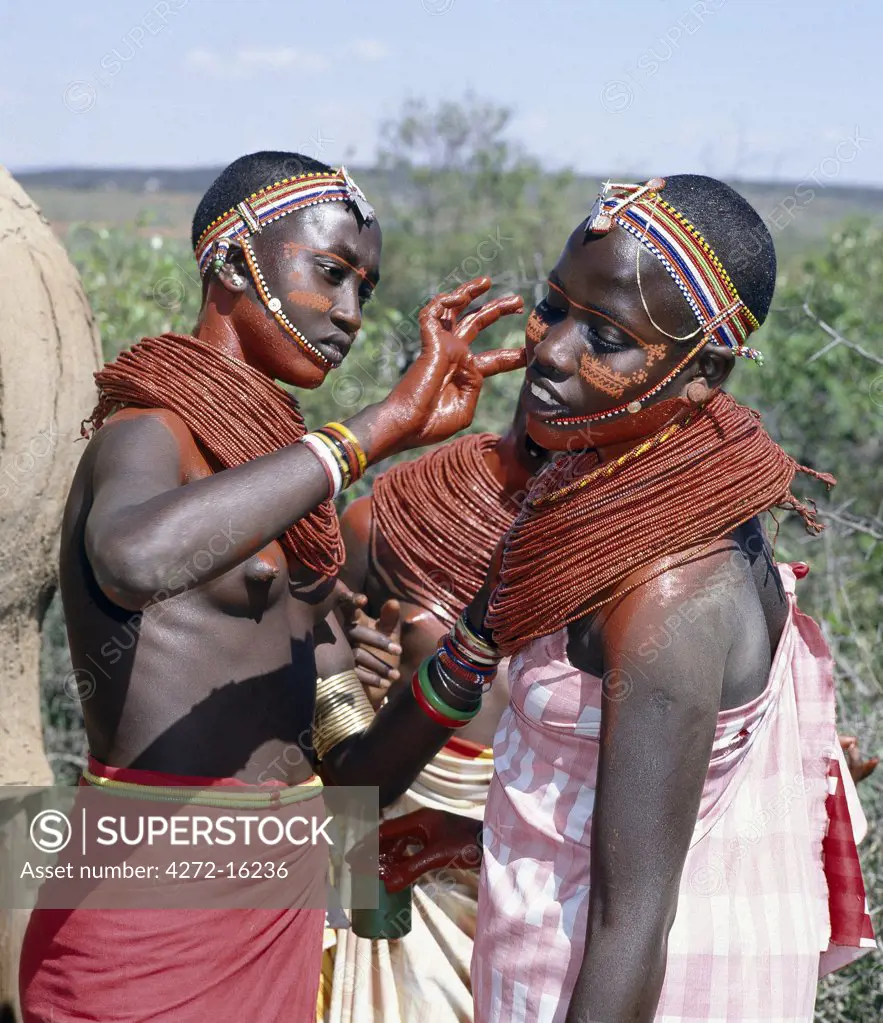 Samburu girls paint each others faces with abstract designs in readiness for a dance.  Already, their necks and beaded necklaces have been coated with red ochre. Only girls and warriors decorate their faces; the orange powder they use is called blue.