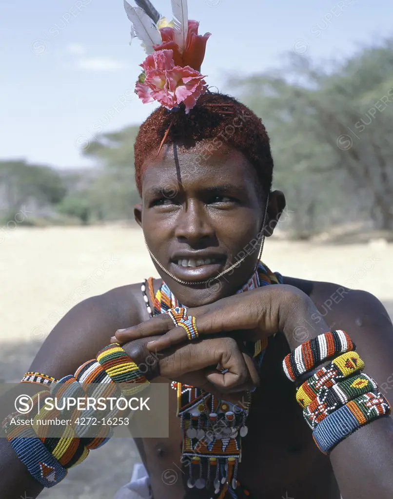 The adornments of Samburu warriors change from generation to generation.  In the 1990's cheap plastic flowers from China became fashionable. This warrior is wearing several bracelets, which bear the Kenyan coat of arms.