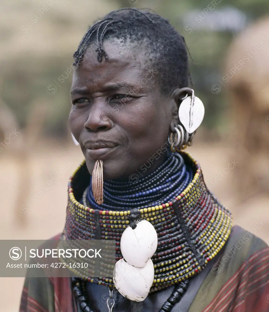 A Turkana woman wears all the finery of her tribe: brass lip plug, beaded collar decorated with bleached shells of the African land snail, leaf-like ear ornaments and metal earrings from which hang tiny rings of goat horn.