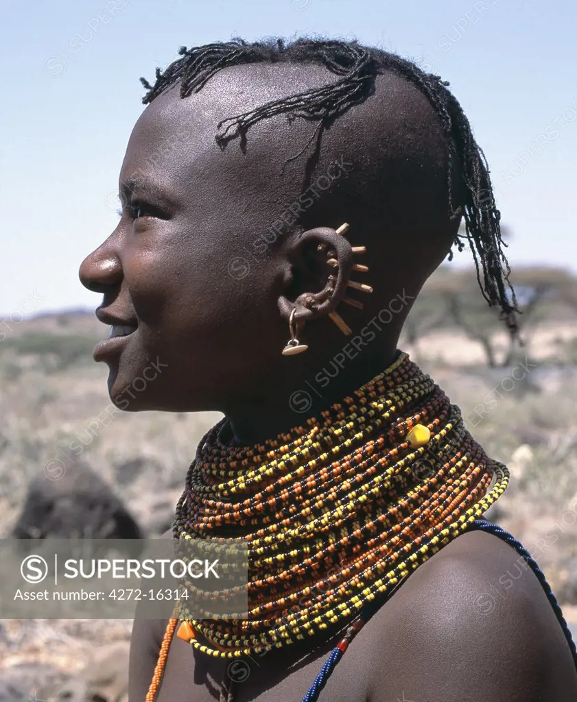 A young Turkana girl has had the rims of her ears pierced in seven places and keeps the holes open with small wooden sticks. After marriage, she will hang leaf-shaped metal pendants from each hole.