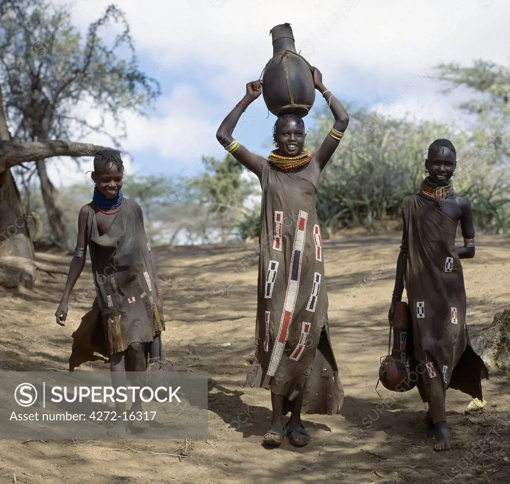 Turkana girls return home from a Waterhole with water containers made of wood. Their cloaks are goatskin embellished with glass beads.