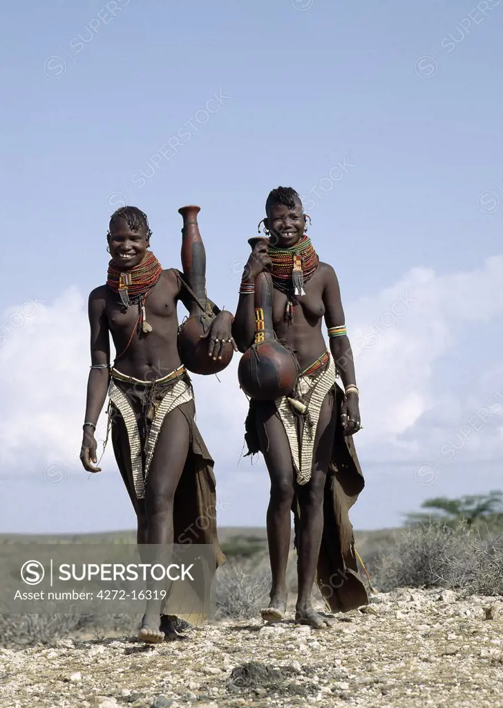 Two Turkana girls set off to fetch water from a nearby Waterhole. Their water containers are made of wood by the women of the tribe.  Their 'V' shaped aprons are made of goatskin and have been edged with hundreds and hundreds of round discs fashioned out of ostrich eggshells.