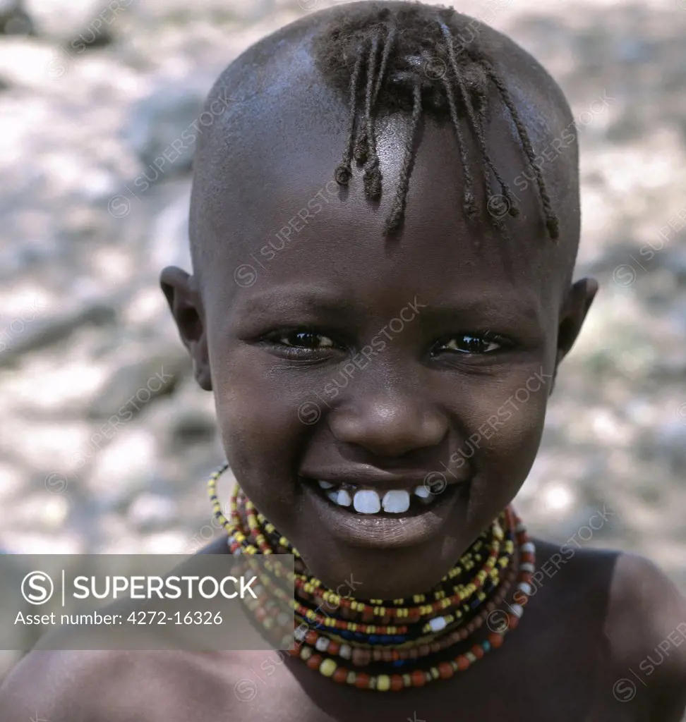 A young Turkana girl with her head shaved except for a tuft, which is braided. This is the usual hairstyle for women and girls.