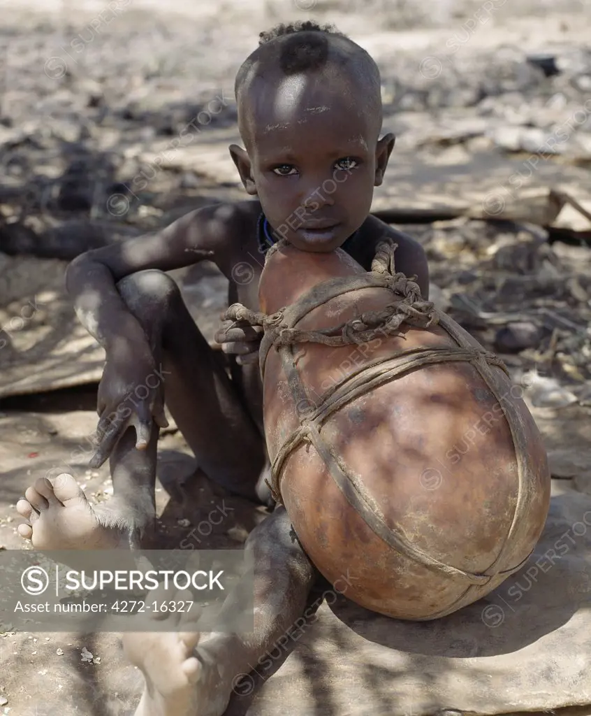 A young Turkana boy looks pensive as he holds a large gourd.  Gourds are less common with the Turkana than the wooden containers their women make; firstly, they are expensive since they have to be brought from afar but more importantly they crack more easily on the move.