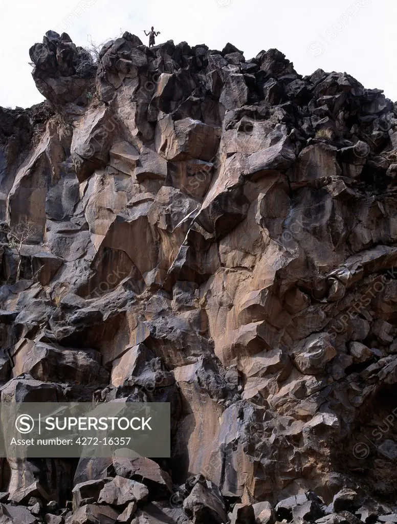 A young Turkana warrior is dwarfed by the sheer cliffs of basaltic lava, bounding the Sirima Gorge.