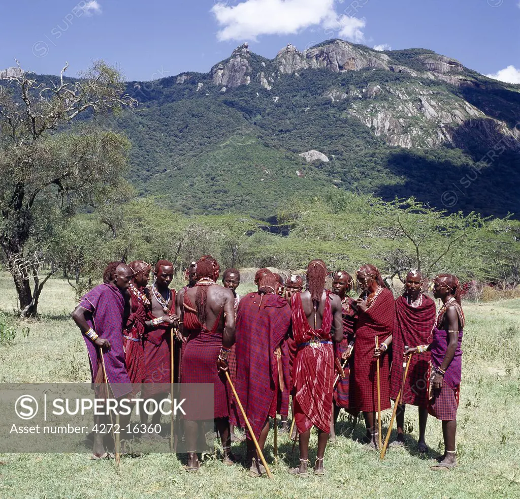 A group of Maasai warriors, resplendent with long Ochred braids, chat beneath Ol doinyo Orok, the black mountain.
